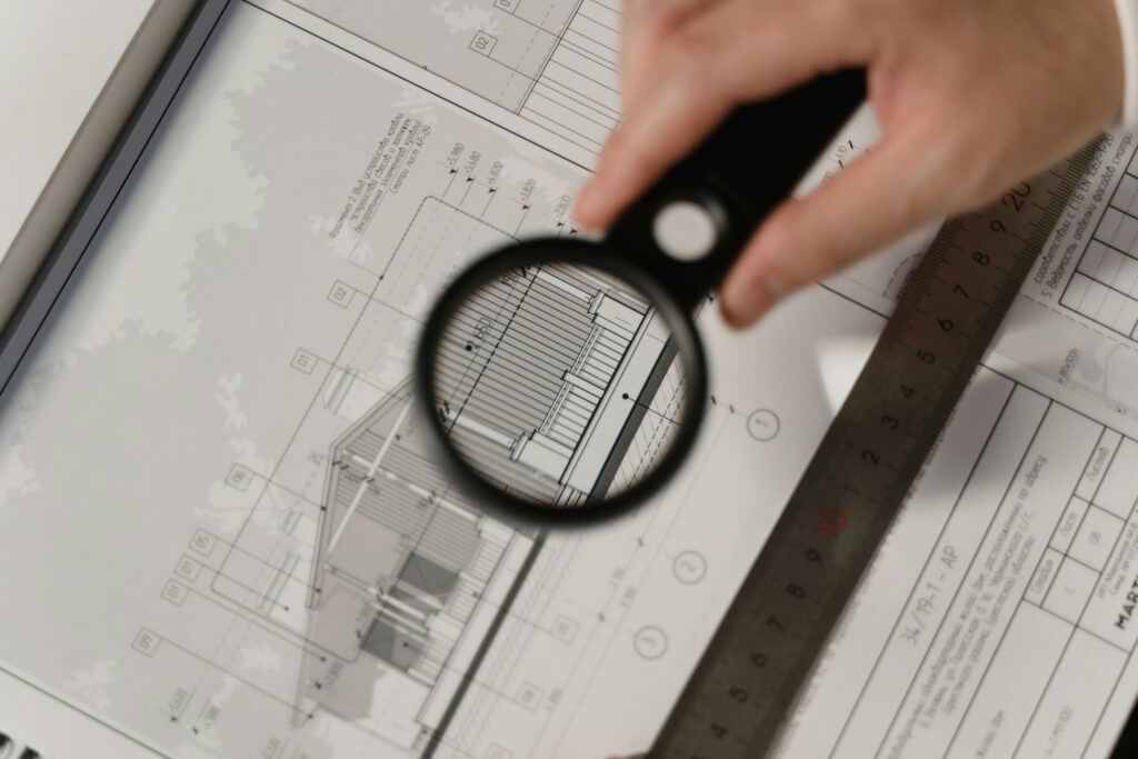 Focused view of architectural plans with magnifying glass, ruler, hands.